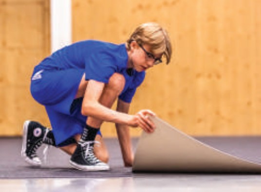 Student laying a gym floor cover tile by hand with no tools